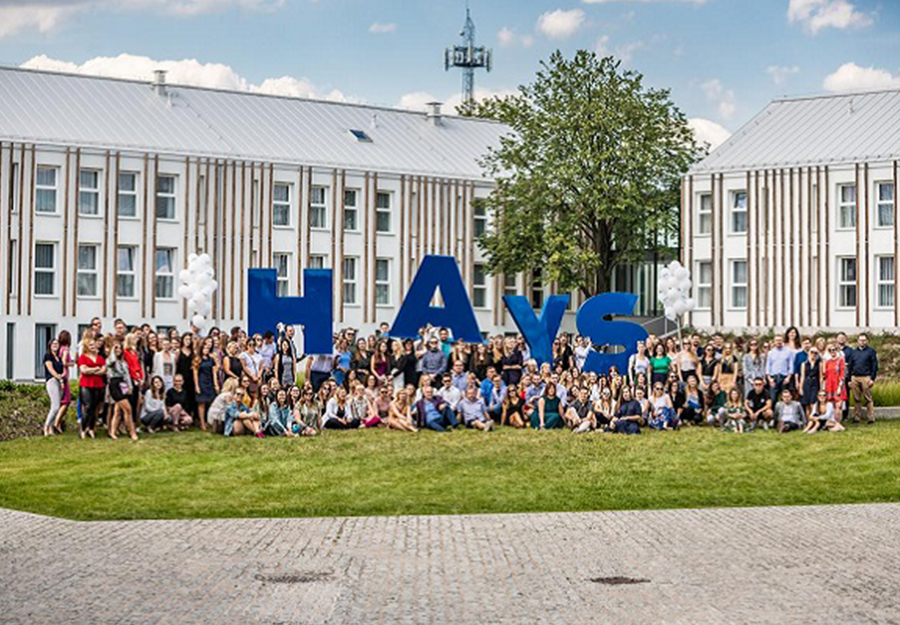 Zdjęcie pracowników Hays Poland na wyjeździe integracyjnym, na tle hotelu. Na zdjęciu widoczny jest napis HAYS trzymany przez pracowników.